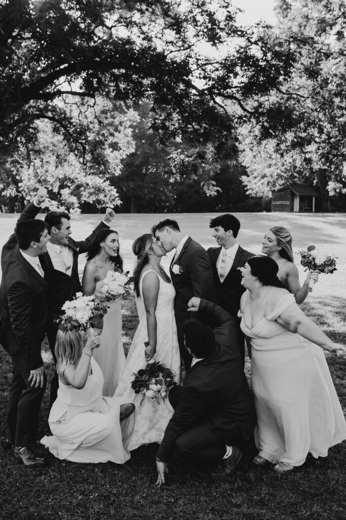 Bridal party pose while bride and groom kiss